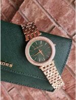 Montre Michael Kors Darci MK3552 en or rose et verte présentée sur un portefeuille au Maroc.