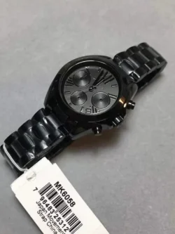 Détails de la montre Michael Kors Mini Bradshaw noire MK6058 tenue en main, montrant l'étiquette.