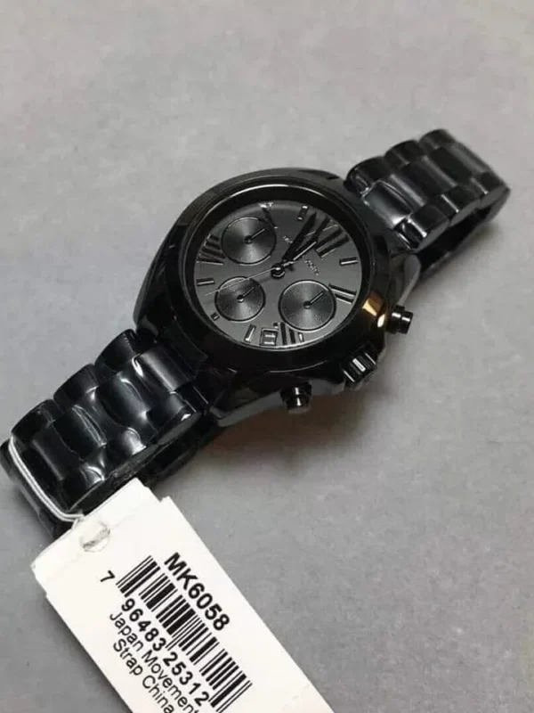 Détails de la montre Michael Kors Mini Bradshaw noire MK6058 tenue en main, montrant l'étiquette.