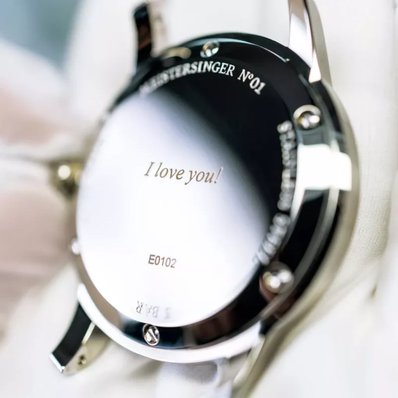 Gros plan sur le dos d'une montre en acier inoxydable avec une gravure "Je t'aime", tenue délicatement dans une main gantée.