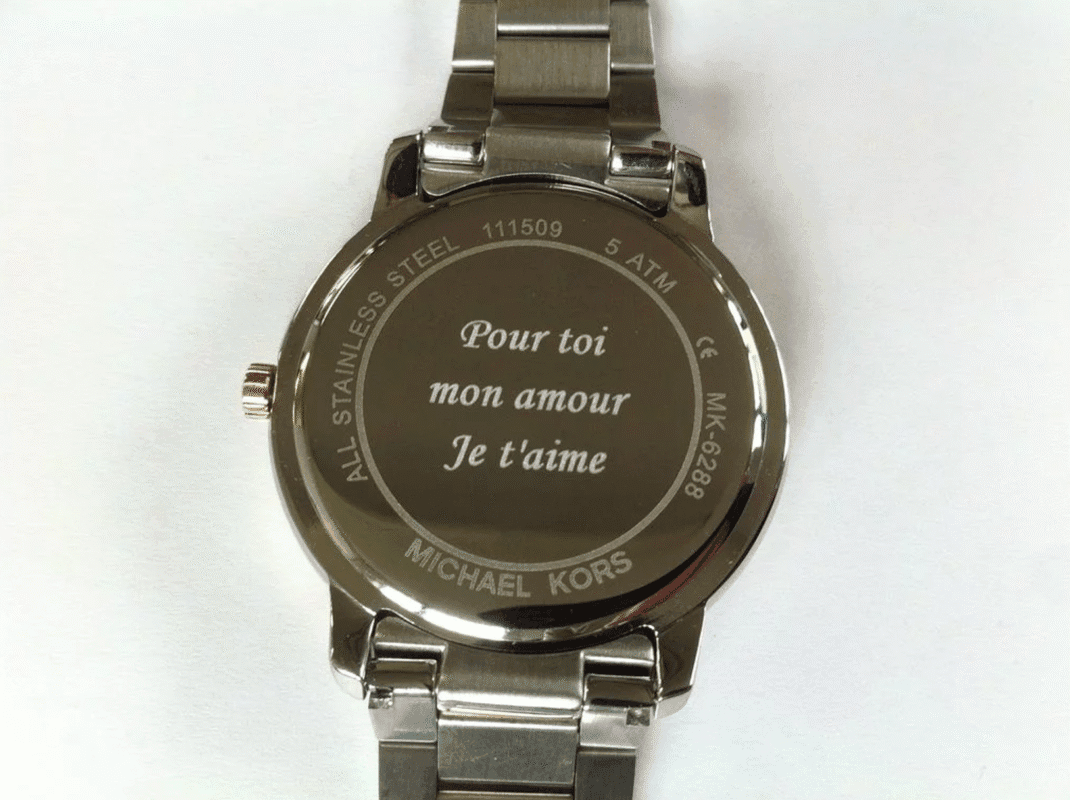 Gros plan sur le dos d'une montre en acier inoxydable avec une gravure "Je t'aime", tenue délicatement dans une main gantée.