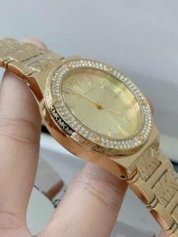 Profil de la montre Michael Kors MK7339 dorée, montrant la lunette à cristaux et la gravure "MK" sur le boîtier.