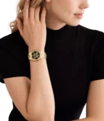 Michael Kors MK7404 portée au poignet d'une femme, bracelet doré et cadran noir élégant