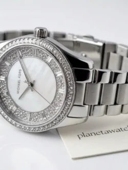 Montre Michael Kors femme argentée posée sur une table en bois avec plante décorative