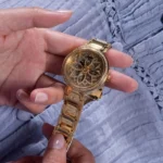 Montre Guess GW0528L2 Lily femme tenue en main, gros plan sur le cadran fleuri serti de strass et le bracelet doré