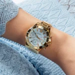 Montre Guess GW0696L2 Phoebe portée au poignet d'une femme en pull bleu ciel, boîtier doré et lunette graduée