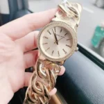 Montre Michael Kors MK3235 Nini femme tenue en main, gros plan sur le boîtier doré et la lunette de cristaux