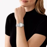 Montre Michael Kors MK4804 Camille portée au poignet d'une femme en haut noir, boîtier argenté serti de cristaux