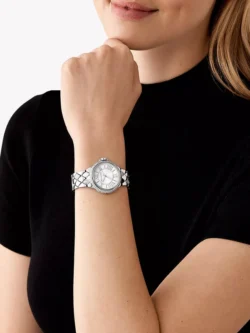 Montre Michael Kors MK4804 Camille portée au poignet d'une femme en haut noir, boîtier argenté serti de cristaux