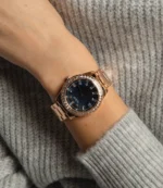 Montre Guess GW0111L3 Sparkler femme portée au poignet sur un pull gris, cadran nacre bleuté et acier or rose
