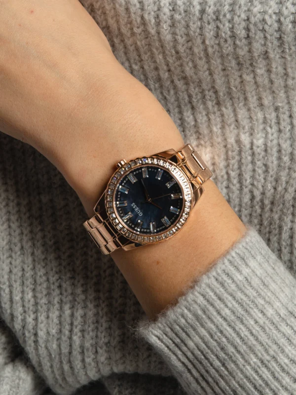 Montre Guess GW0111L3 Sparkler femme portée au poignet sur un pull gris, cadran nacre bleuté et acier or rose