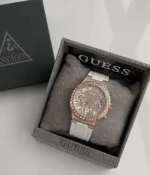 Guess GW0257L2 présentée sur le coussin gris de son écrin Guess, cadran blanc et boîtier or rose étincelants
