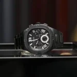 Montre Guess GW0572G3 Headline noire vue de trois quarts sur une surface miroir, cadran à chiffres romains blancs