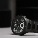 Montre Guess GW0572G3 couchée sur le côté, lunette noire à vis et bracelet à maillons en acier noir