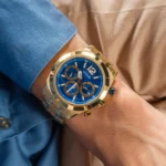 Guess GW0714G2 portée au poignet d'un homme en chemise bleue, cadran bleu et bracelet acier doré