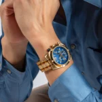 Homme en chemise en jean portant la Guess GW0714G2 dorée, mains croisées, cadran bleu bien visible