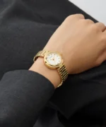 Montre Guess GW0930L2 femme dorée portée au poignet sur un pantalon gris, cadran blanc et bracelet doré
