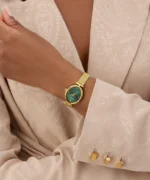 Montre Guess GW0935L2 femme au poignet avec une veste beige, boîtier ovale doré et cadran vert