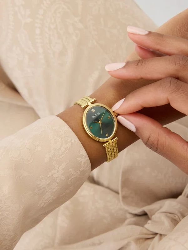 Montre Guess GW0935L2 femme portée au poignet, cadran vert sur boîtier ovale doré et bracelet maille