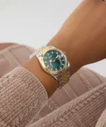 Montre Guess GW0936L3 Jada femme au poignet d'une femme assise, cadran vert et bracelet bicolore argent et or
