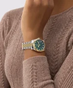 Montre Guess GW0936L3 femme portée au poignet sur un pull en maille marron, cadran vert et lunette dorée