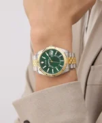 Montre Guess GW0977G4 homme portée au poignet avec une veste beige, cadran vert et lunette cannelée dorée