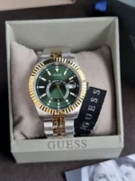 Montre Guess GW0977G4 Jaden homme posée dans une boîte Guess, cadran vert, lunette dorée et bracelet bicolore