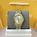 Michael Kors MK3456 dorée posée sur le coussin de son écrin Michael Kors, sac jaune de la marque en arrière-plan