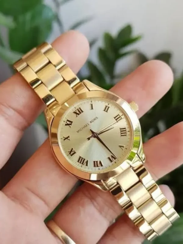 Michael Kors MK3456 tenue en main devant des plantes vertes, cadran doré soleillé avec chiffres romains