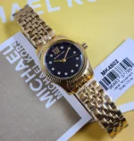 Michael Kors MK4802 dorée posée sur son étiquette, cadran sombre pailleté à index en cristaux et chiffre XII