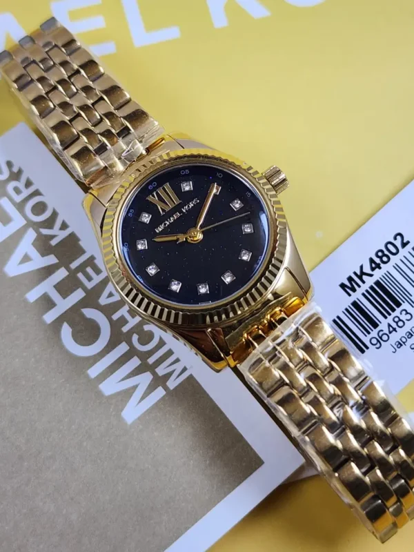 Michael Kors MK4802 dorée posée sur son étiquette, cadran sombre pailleté à index en cristaux et chiffre XII