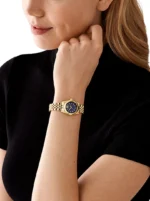 Femme en haut noir portant la Michael Kors MK4802 dorée au poignet, main posée près du menton