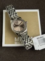 Michael Kors MK4843 posée sur sa boîte avec son étiquette, lunette cannelée argentée et cadran crème