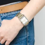 Michael Kors MK4935 portée au poignet d'une femme en jean, boîtier carré et bracelet à maillons argent et or