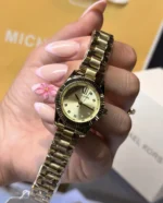 Montre Michael Kors MK4951 tenue en main, cadran doré soleillé avec chiffre romain XII et index en cristaux