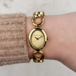 Michael Kors MK4957 portée au poignet avec un pull beige, cadran doré ovale et logo Michael Kors visibles