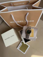 Michael Kors MK4986 présentée dans son écrin devant le sac et la boîte Michael Kors, cadran vert à cristaux