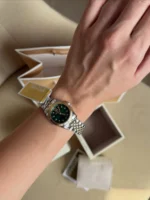Michael Kors MK4986 portée au poignet d'une femme, cadran vert et lunette cannelée dorée, boîtes en arrière-plan