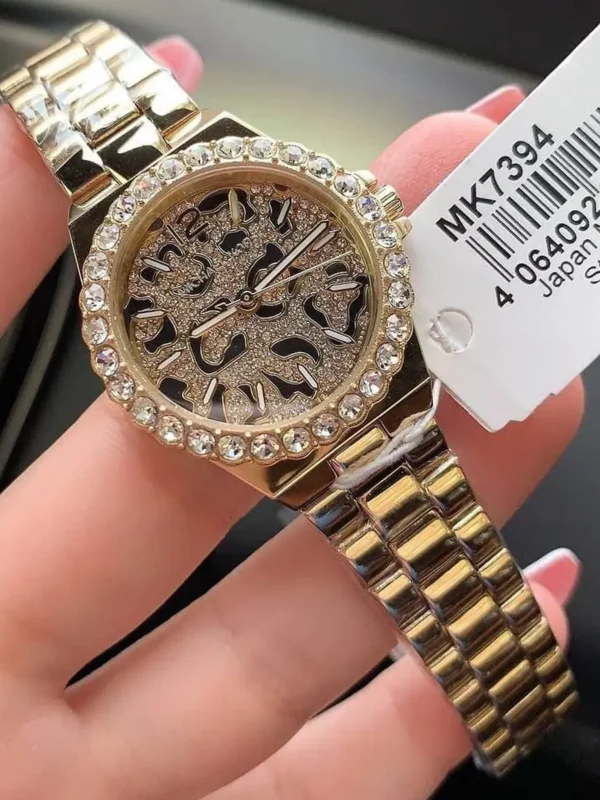 Montre Michael Kors MK7394 tenue dans la main avec son étiquette, cadran léopard et bracelet en acier doré