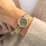 Montre Michael Kors MK7394 portée au poignet d'une femme en pull beige, lunette de cristaux et bracelet doré