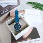 Michael Kors MKO1004 présentée dans son écrin blanc Michael Kors, bracelet en silicone bleu à logo MK déployé à côté.