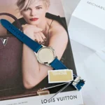 Dos du boîtier en acier de la Michael Kors MKO1004 posé sur un magazine, bracelet en silicone bleu à motif logo MK visible.