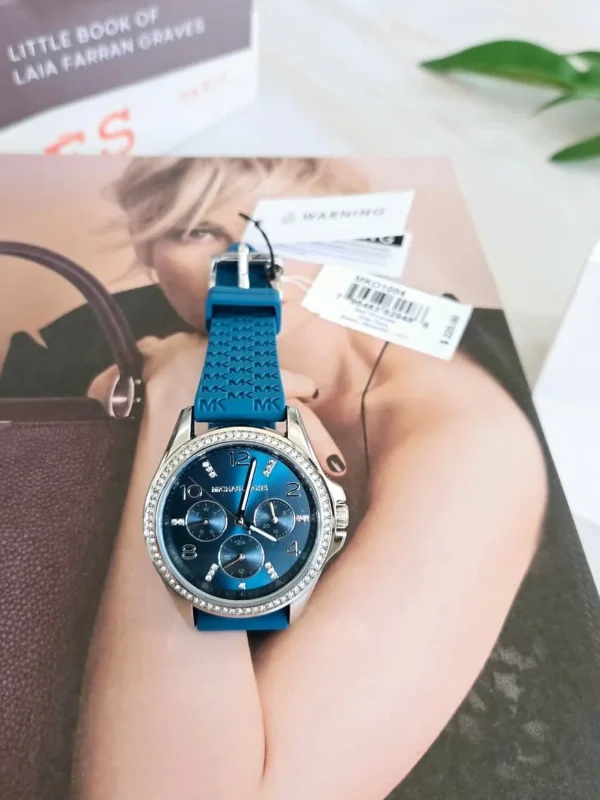 Michael Kors MKO1004 posée sur un magazine, cadran bleu chronographe et étiquettes de la marque encore attachées au bracelet.