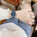 Michael Kors MKO1004 portée au poignet, cadran bleu chronographe et lunette pavé visibles sous une manche blanche.