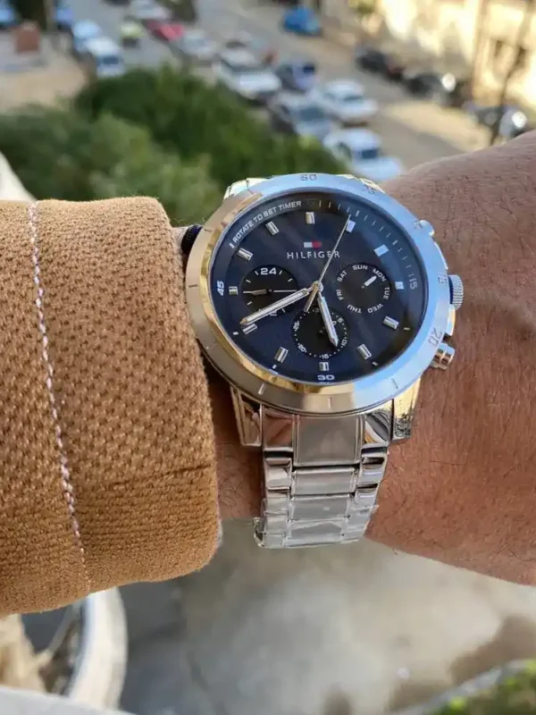 Montre Tommy Hilfiger 1792104 Troy homme portée au poignet avec un pull camel, cadran bleu et bracelet acier
